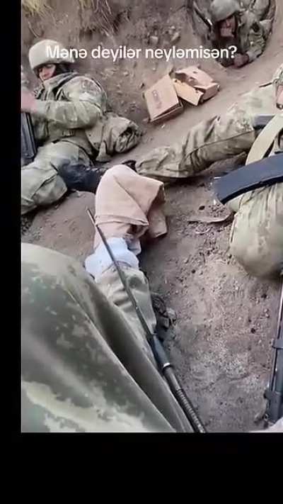 Russian soldiers sitting in a trench as drones buzz overhead.