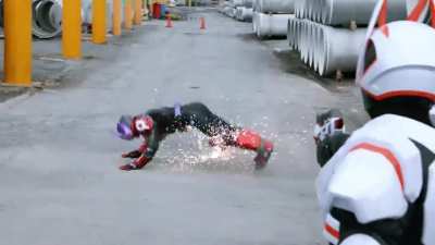Kamen Rider wiggles on the ground to avoid gunshots
