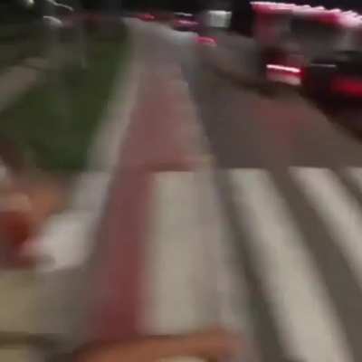 Guy on bike helps an old lady cross a busy street at night by stopping traffic.