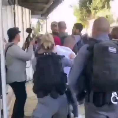 A man shields an elderly Palestinian woman from Israeli Occupation Forces who push them out to make way for Israelis participating in today's 