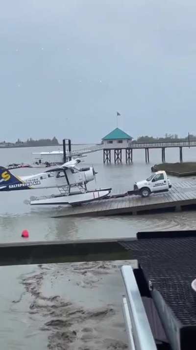 Half of a truck towing an airplane up a boat ramp
