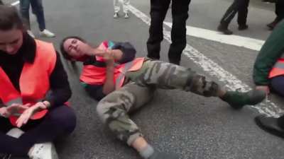 Climate activist reacts theatrically as his glued hand is gently pulled off the road.