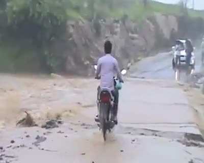 Man riding bike pushes through an overflowing river, gets washed away with it.