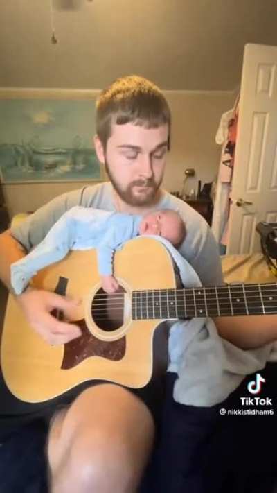 Baby chilling on a guitar while dad plays it