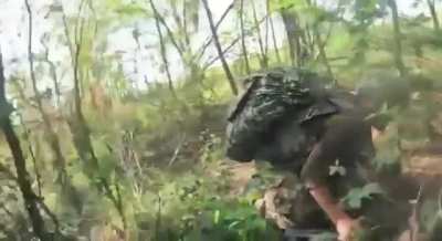GoPro footage of a Russian soldier and his comrade hiding out in a wooded area as an FPV drone approaches them and explodes close by