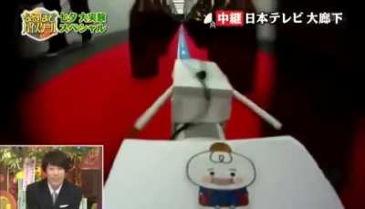Japanese contestant places various sized bottles in a pattern along a model train path to bang out a classic tune