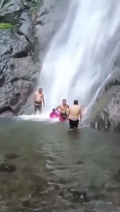 Waterfall drops dirt with rocks and other debris on people relaxing and bathing