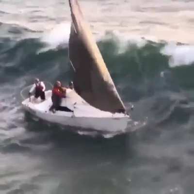 Tiny sailboat tumbles over by the breaking wave coming upon the land