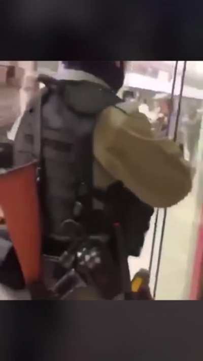 After tear gassing himself, a riot policeman takes a bottle of water from a shop and leaves without paying.