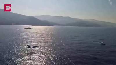 Turkish Air Force F-16 fighter jet passing at extremely low altitude over a ship at the sea.