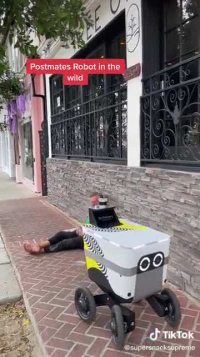 Homeless man watches a food delivery robot drive by