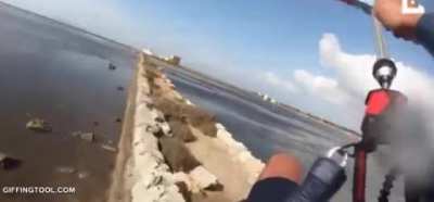 Kitsurfer tries and fails to jump over a median of pointy rocks
