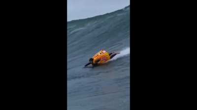 A man rides a huge wave using a customized inflatable surf vest.