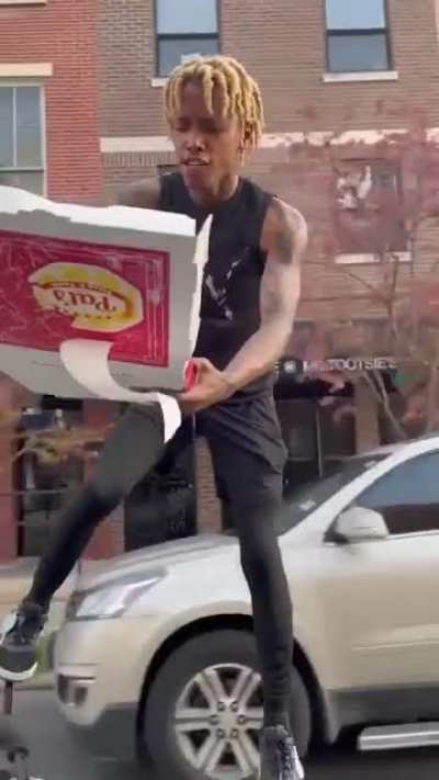 Riding a bike by standing on it, steering with one leg whilst eating pizza.