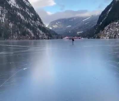 man using an umbrella, like Mary Poppins, as he and his friends skate on Three Valley Lake near Revelstoke