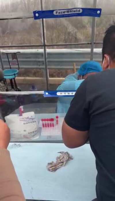 A nucleic acid test station worker casually smoking a cigarette, mask down, blowing smoke down people’s throats and sneez<wbr>ing😅🤣
