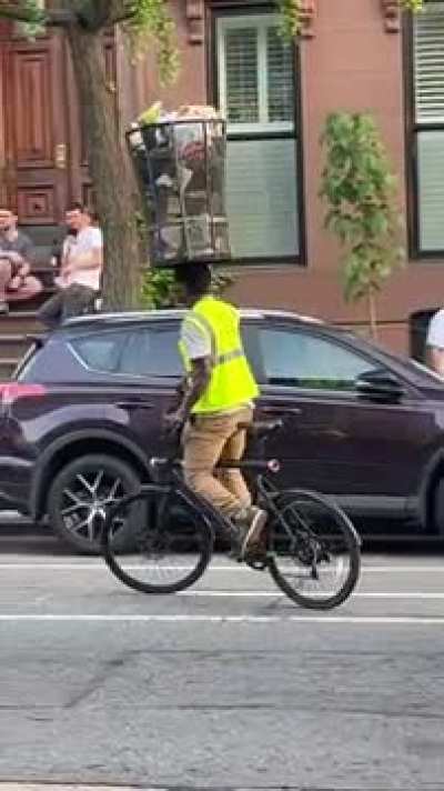 Man balances a full NYC trashcan on his head while cycling
