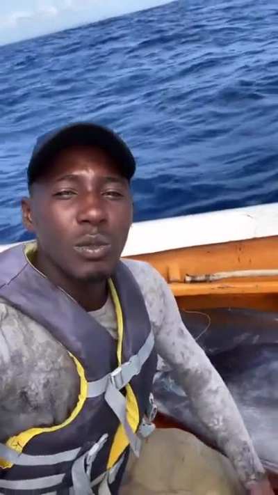 Jamaican fisherman reels in a Blue Marlin entirely on his own. Fish takes up more than half the length of his boat.