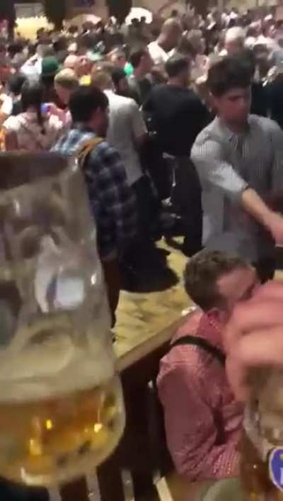 man pisses on floor at oktoberfest, hitting another man’s leg and making a bar-maiden slip and eat piss