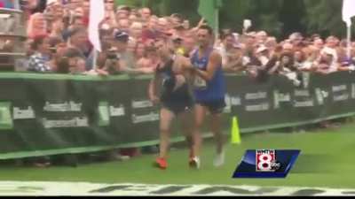 Collapsed first place runner is helped across the line by second place runner.
