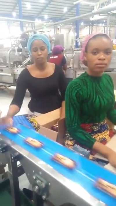 Workers at a biscuit company shows their mastery of filling a carton of biscuit
