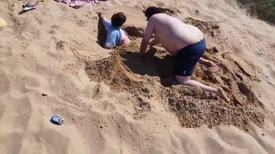 Two Bri’ish guys dig a hole while a third Bri’ish guy films them with a drone
